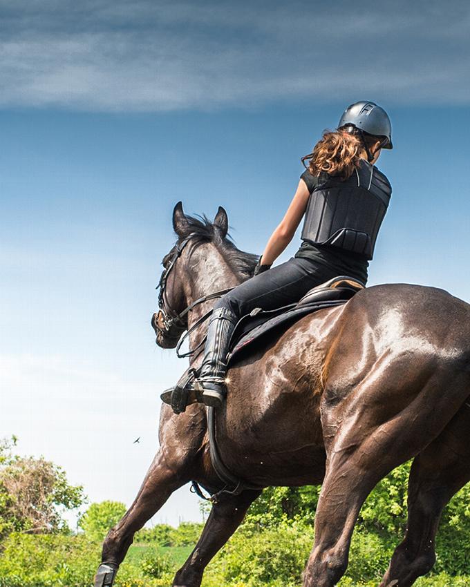 Back view of woman wearing safety gear while horse riding